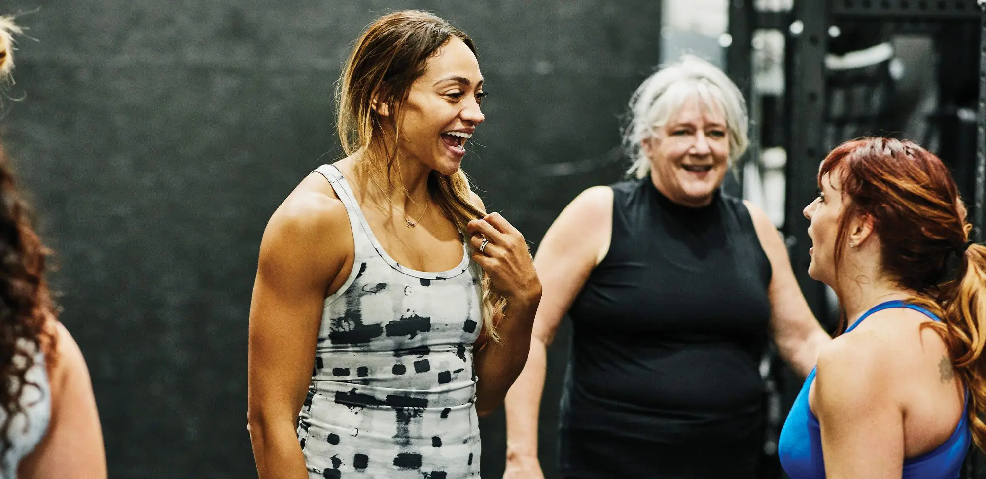 Smiling fitness instructor in discussion with clients during class in gym