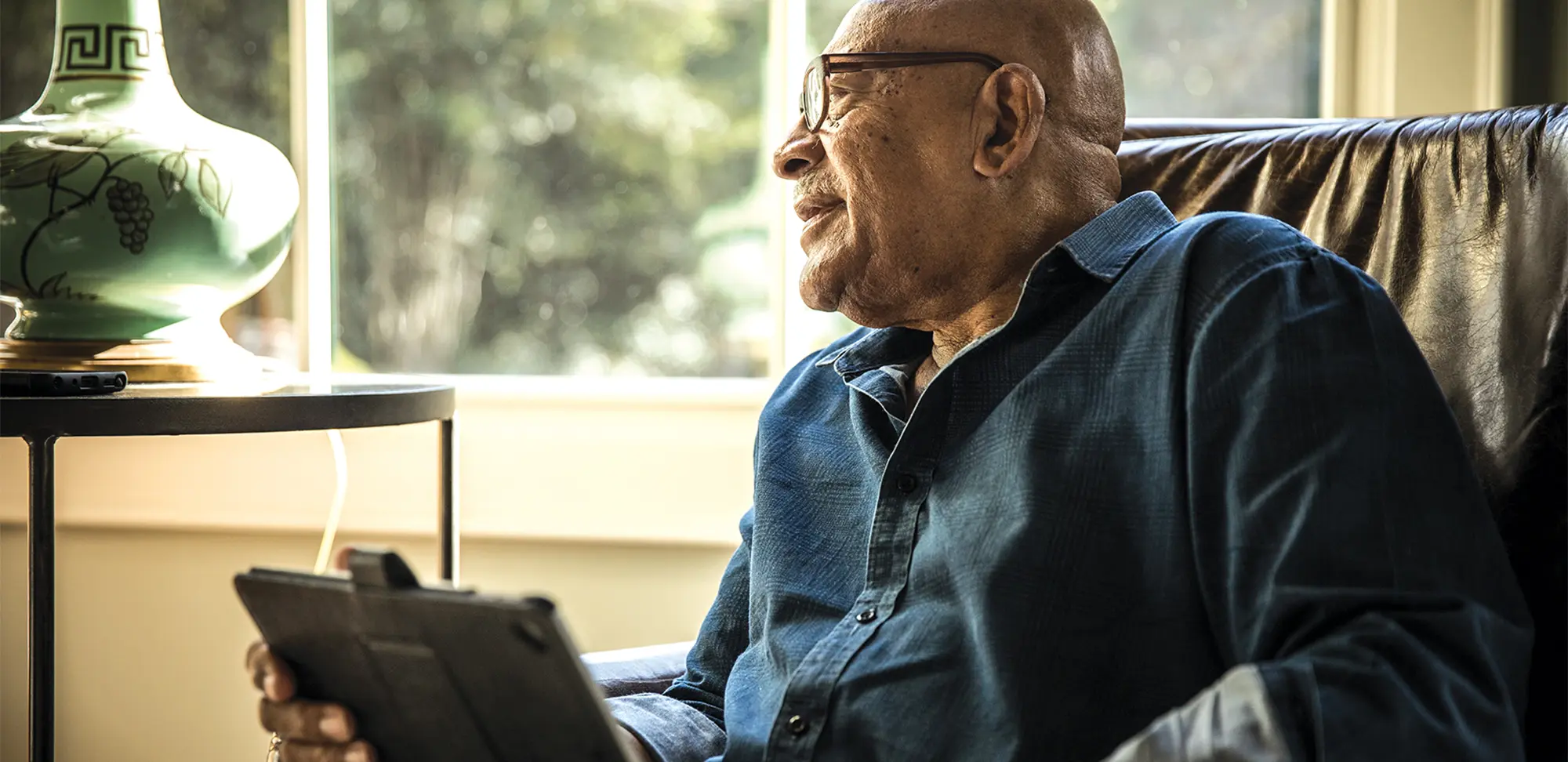 Photo of a man sitting in a chair by a window holding a mobile device.