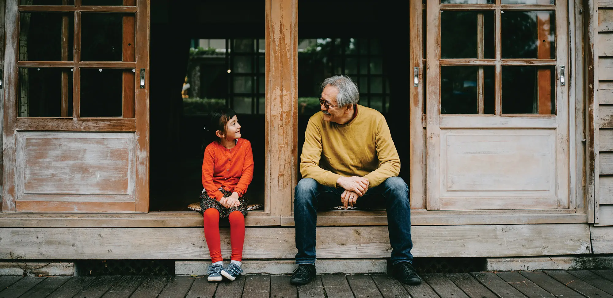 Grandfather and granddaughter sitting on patio and smiling at each other