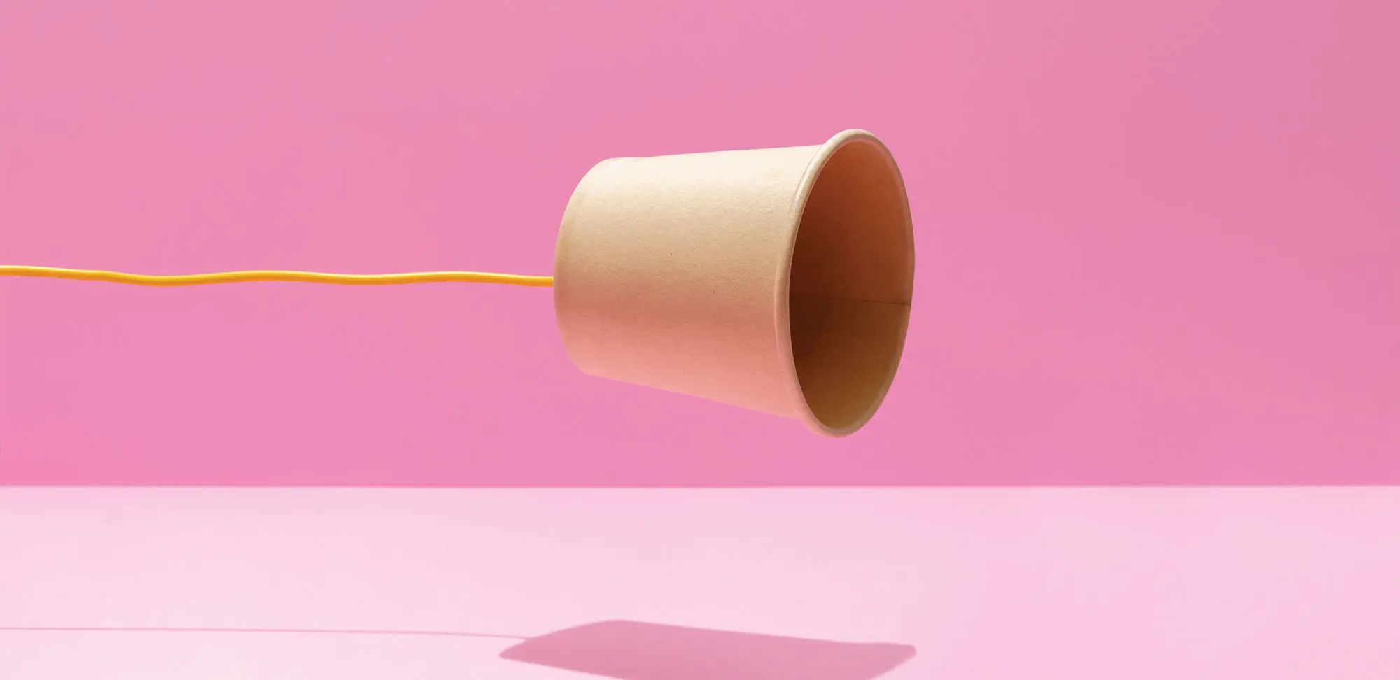 Photo of paper cup united with a yellow string on a pink background. Communication concept