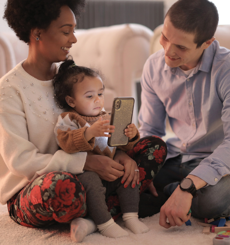 Photo of parents and a baby holding a smart phone at home