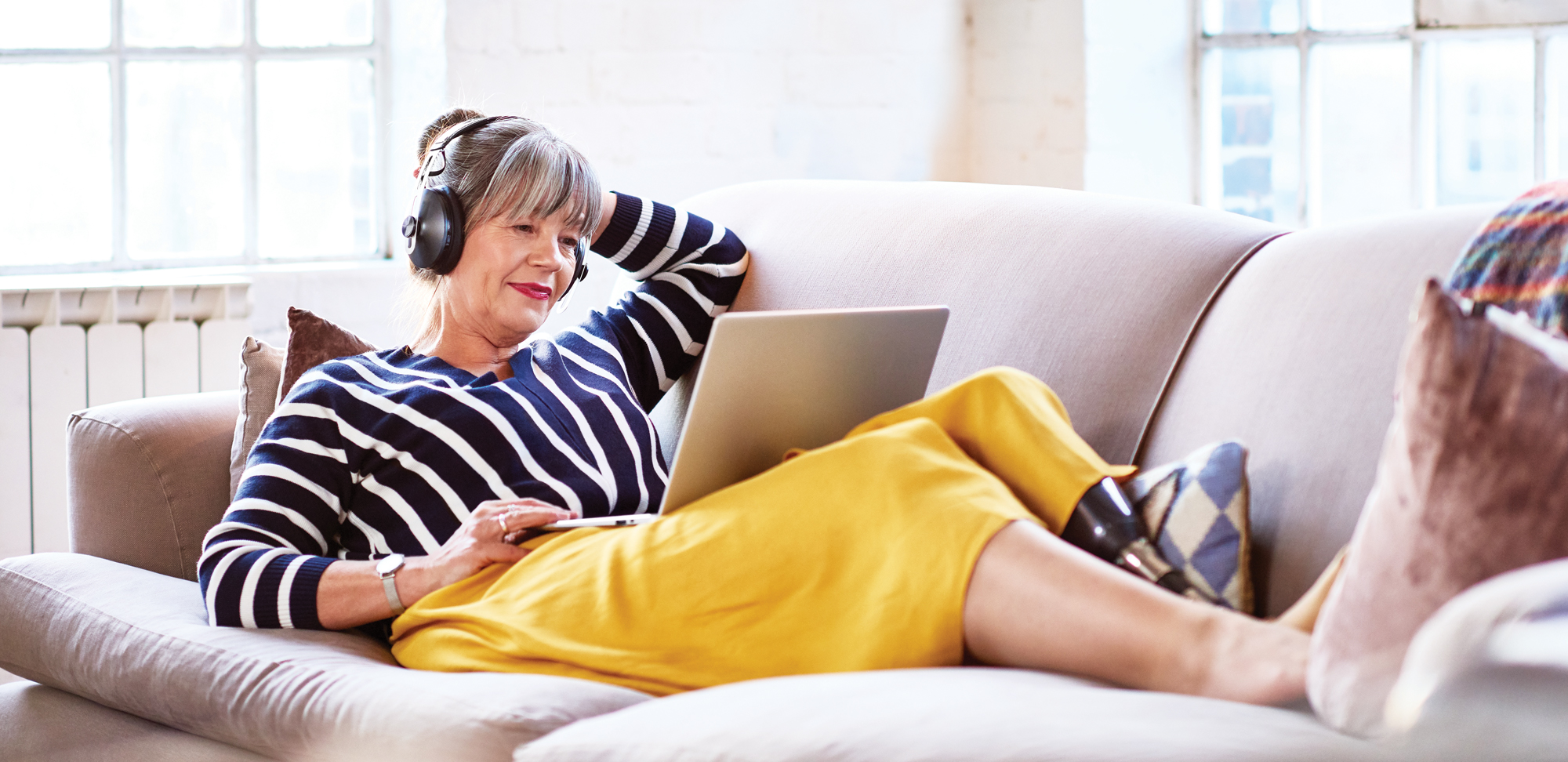 Photo of a senior woman wearing headphones watching movie on laptop