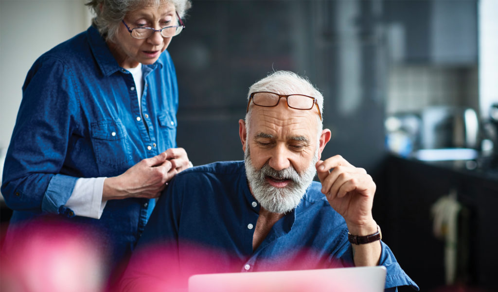 Photo of a senior man with beard using laptop and woman watching