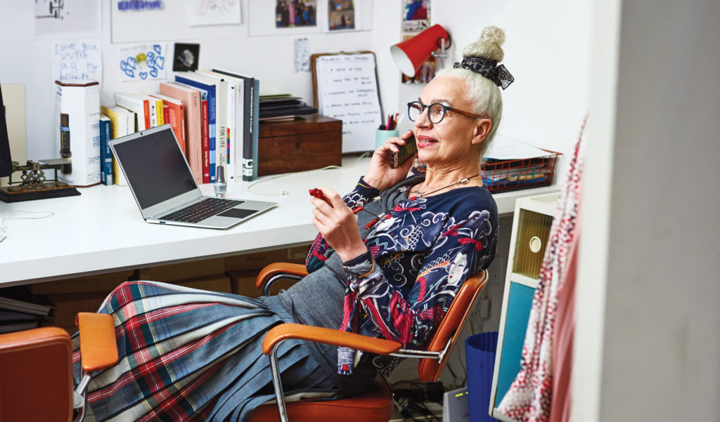 Photo of a woman in her 60s sitting at desk on phone call with laptop