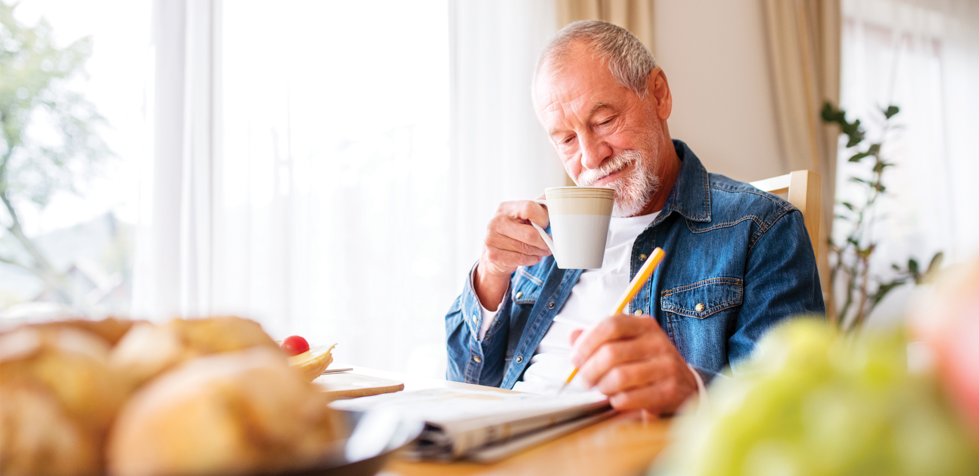 Photo of a senior man drinking a cup of coffee doing crosswords