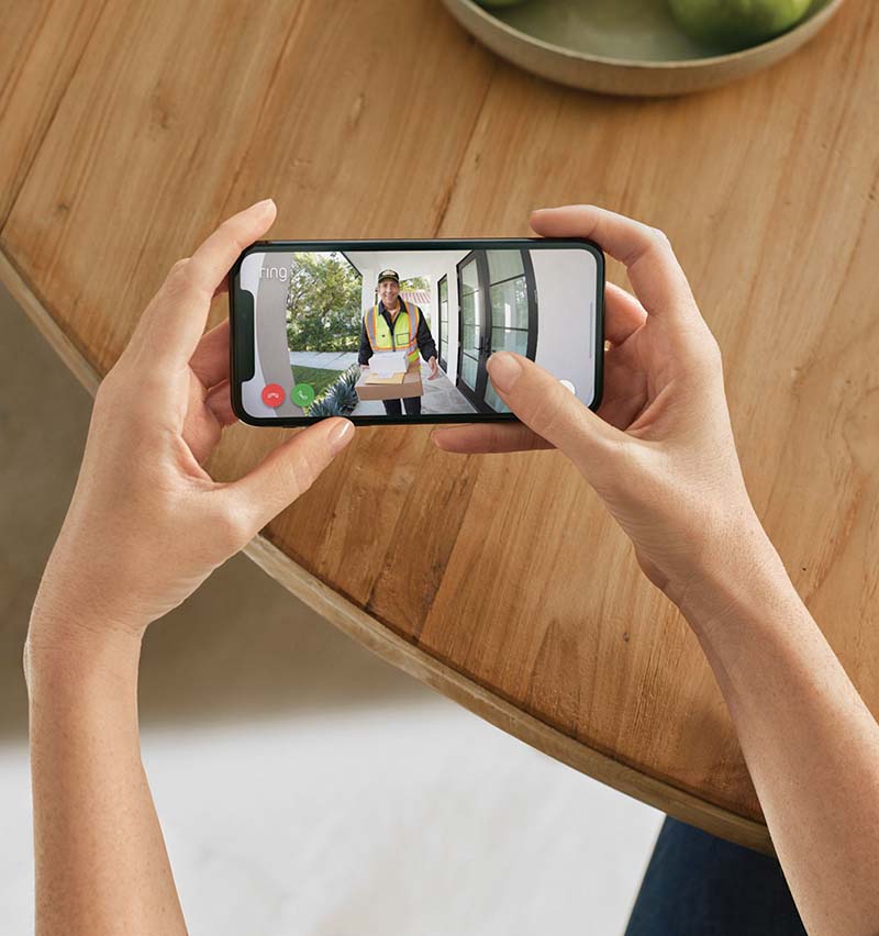 Photo of woman holding smartphone using the doorbell camera system Ring