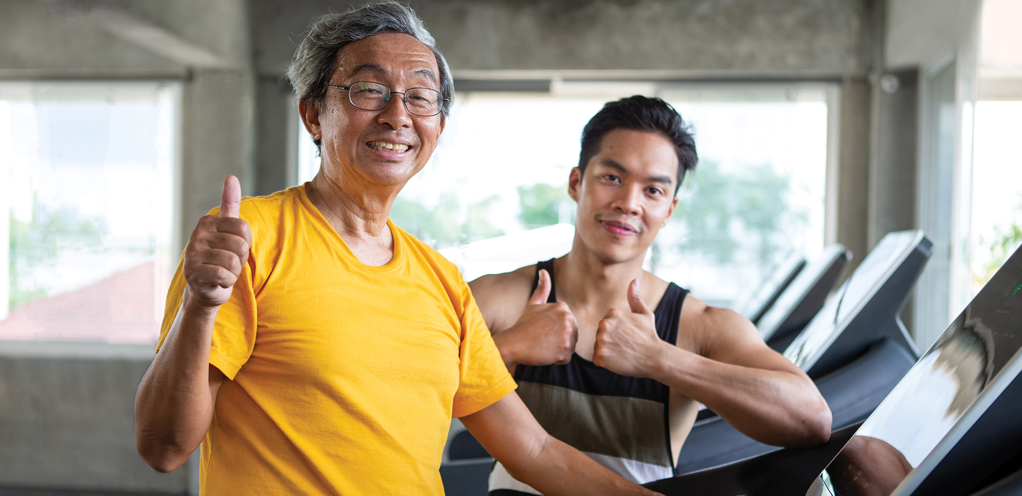 Photo of an Asian senior man on a treadmill with Personal trainer in fitness gym