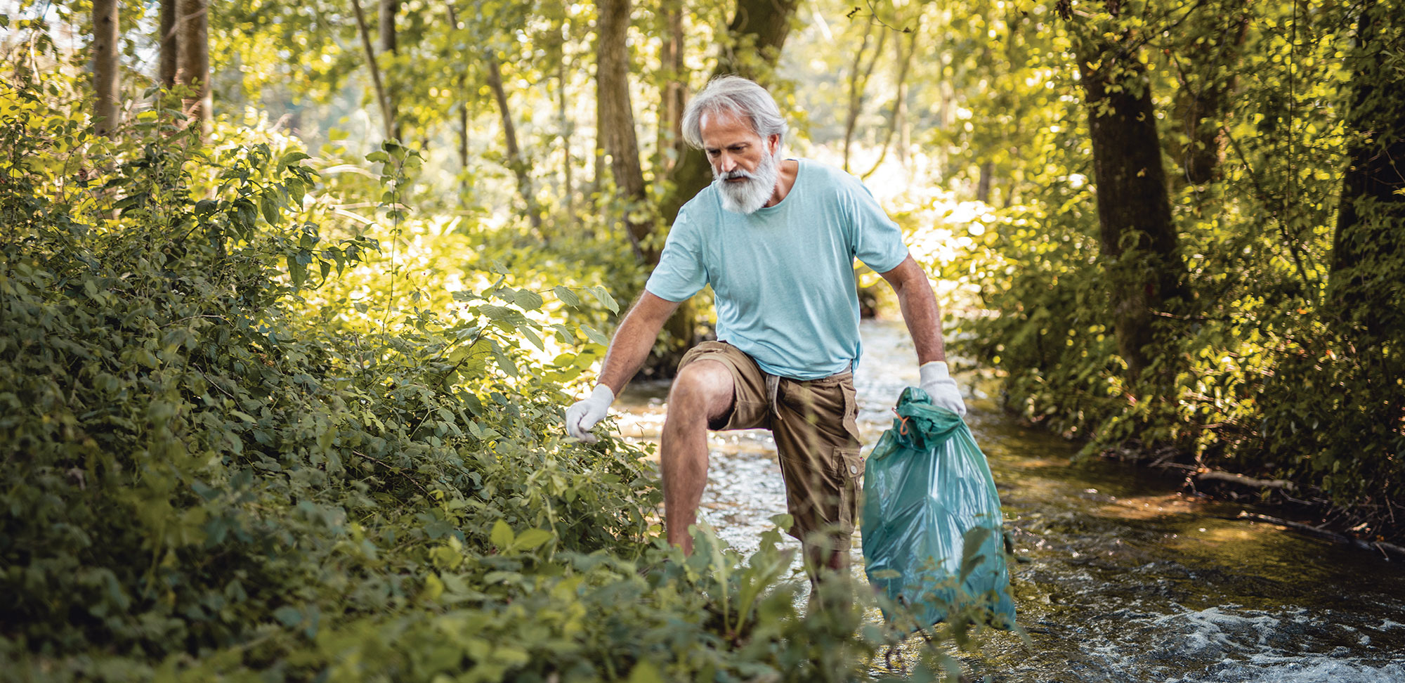 Photo d’un aîné qui s’active à ramasser les déchets d’un ruisseau dans un parc