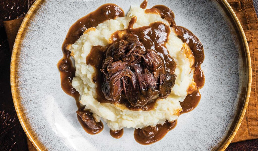 Photo of Slow cooked beef cheeks in red wine sauce with mashed potato. Dark background.