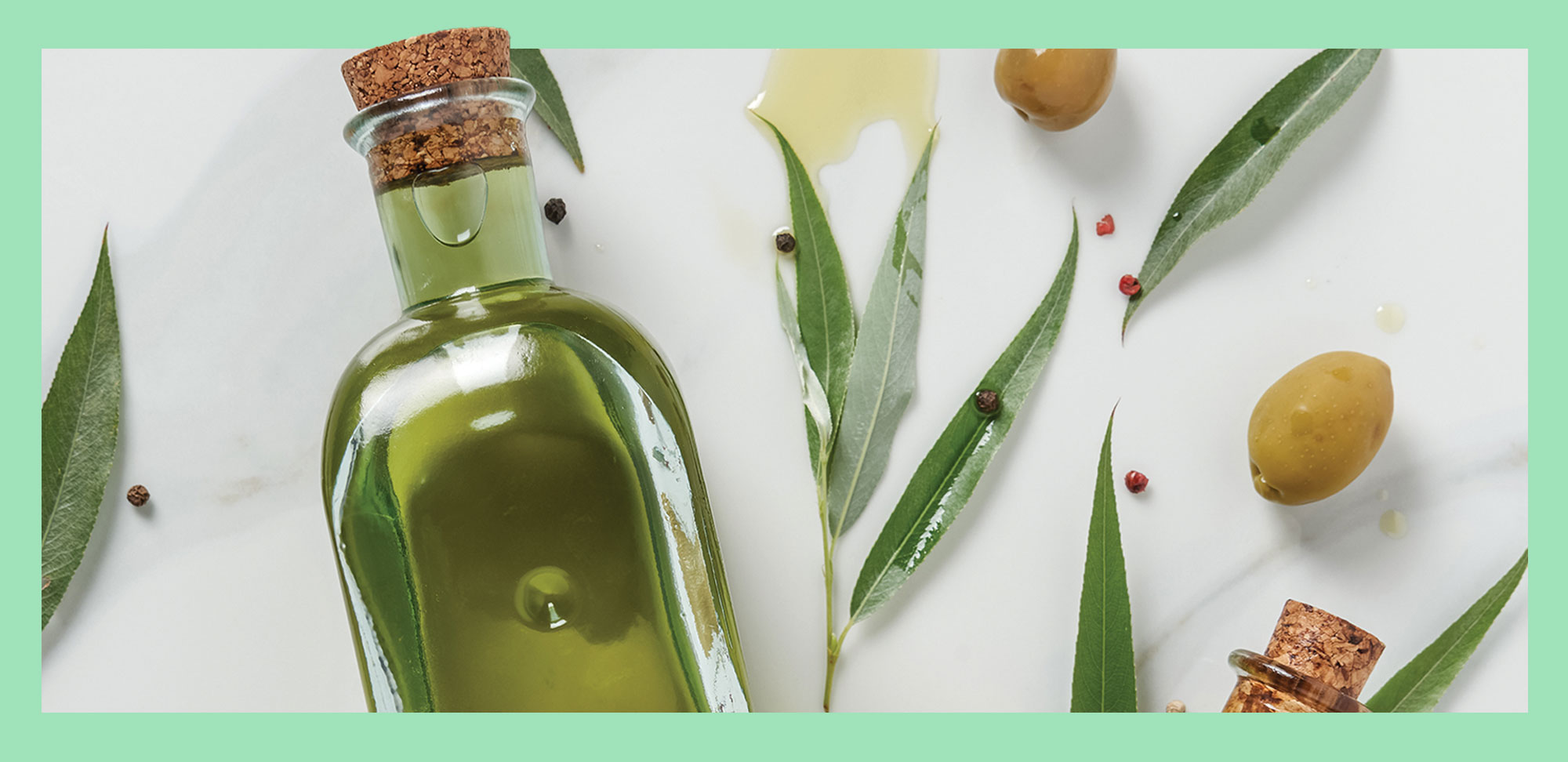 Photo de la partie supérieure de deux bouteilles d’huile d’olive et de feuilles sur une table en marbre